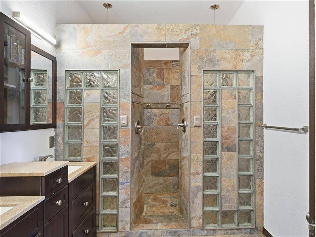 1039 Wood Brook Drive, Grand Prairie, TX 75052 Walk-in shower featuring natural stone-look tile, glass block partitions, and dual shower controls