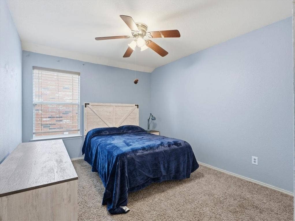 1039 Wood Brook Drive, Grand Prairie, TX 75052 Carpeted bedroom featuring a window with blinds, a wood-finish ceiling fan with lighting, and light blue wall paint