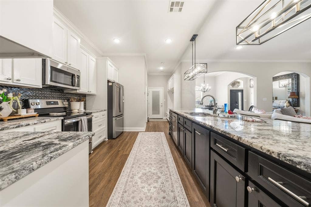 386 Cavitt Court, Robinson, TX 76706 Kitchen featuring an expansive island with a light-toned countertop, stainless steel appliances, white upper cabinetry, dark lower cabinetry, and wood-finish flooring