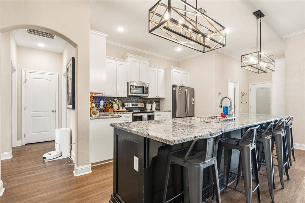 386 Cavitt Court, Robinson, TX 76706 Kitchen featuring a large central island with seating, pendant lighting, stainless steel appliances, white cabinetry, and wood-finish flooring