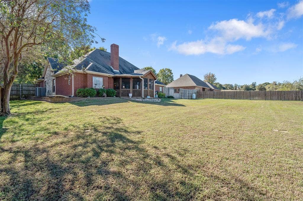 126 E Post Oak, Frankston, TX 75763 Expansive backyard featuring a large green lawn, a wooden privacy fence, and a brick and stone exterior home with a screened porch