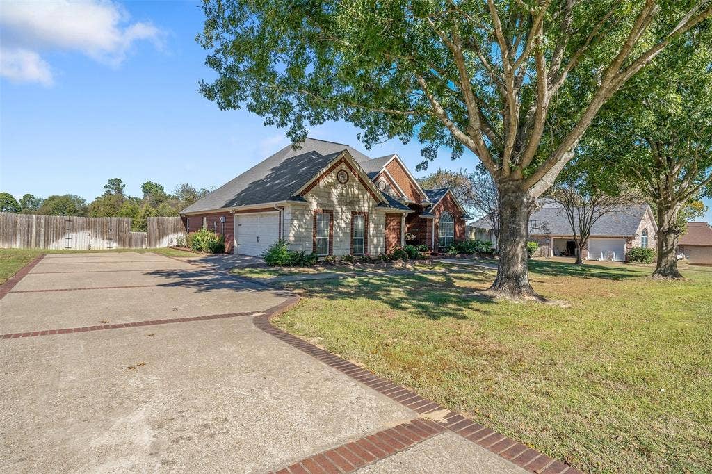 126 E Post Oak, Frankston, TX 75763 Spacious concrete driveway with brick accents, two-car garage, brick and stone exterior, mature trees, and a wooden privacy fence