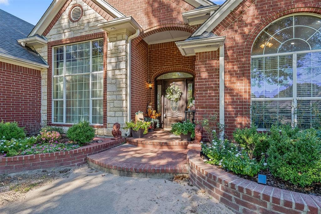 126 E Post Oak, Frankston, TX 75763 Brick and stone facade featuring a prominent arched entry, large picture windows, and a curved brick planter