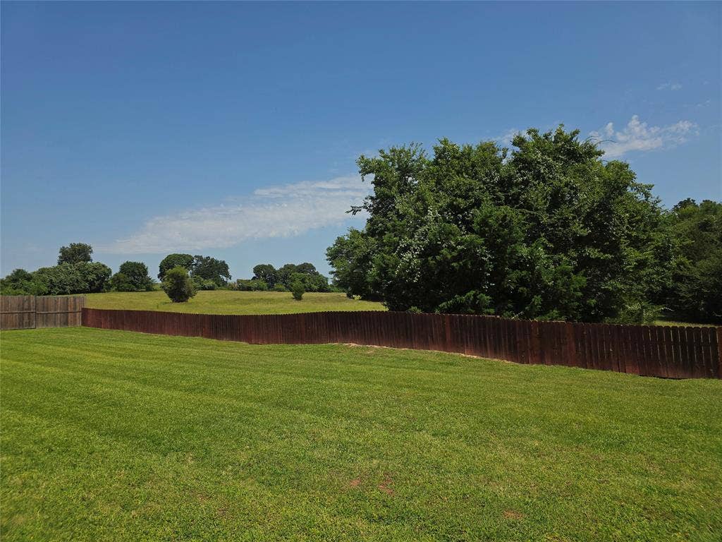 126 E Post Oak, Frankston, TX 75763 Expansive green lawn with a perimeter wood fence, bordered by mature trees and open fields