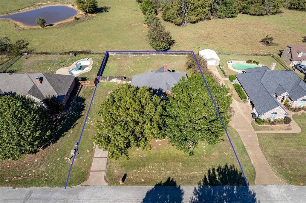 126 E Post Oak, Frankston, TX 75763 Aerial view showcasing the property's footprint with a spacious backyard, mature trees, and a pond beyond the rear boundary