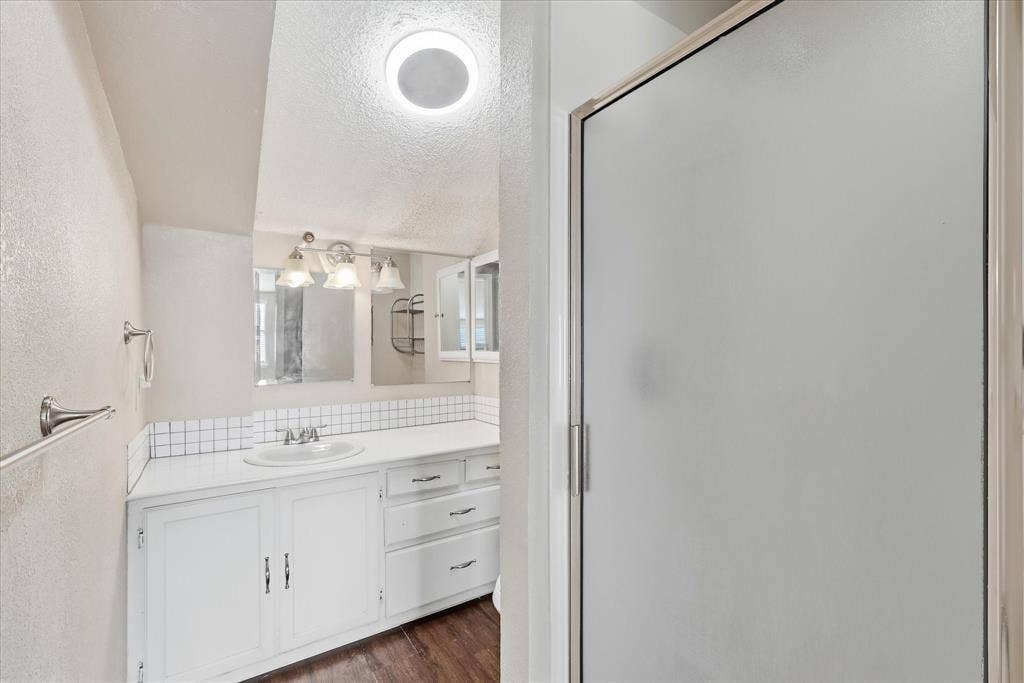 6505 Hughes Drive, Watauga, TX 76148 Bathroom featuring a white vanity with integrated sink, white tile backsplash, and wood-finish flooring