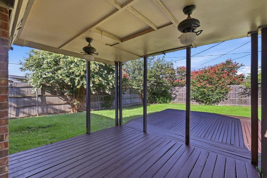6505 Hughes Drive, Watauga, TX 76148 Covered outdoor deck with ceiling fans, dark-stained wood-finish decking, and a fenced backyard with mature trees