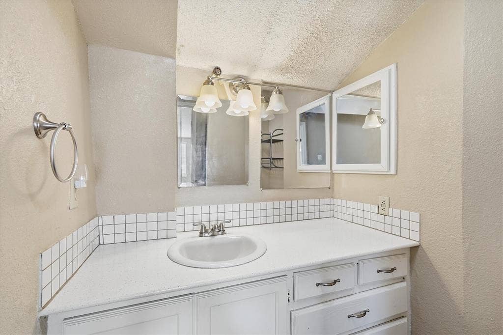 6505 Hughes Drive, Watauga, TX 76148 Bathroom vanity featuring a white countertop with an integrated sink, white base cabinetry, and a mirrored medicine cabinet