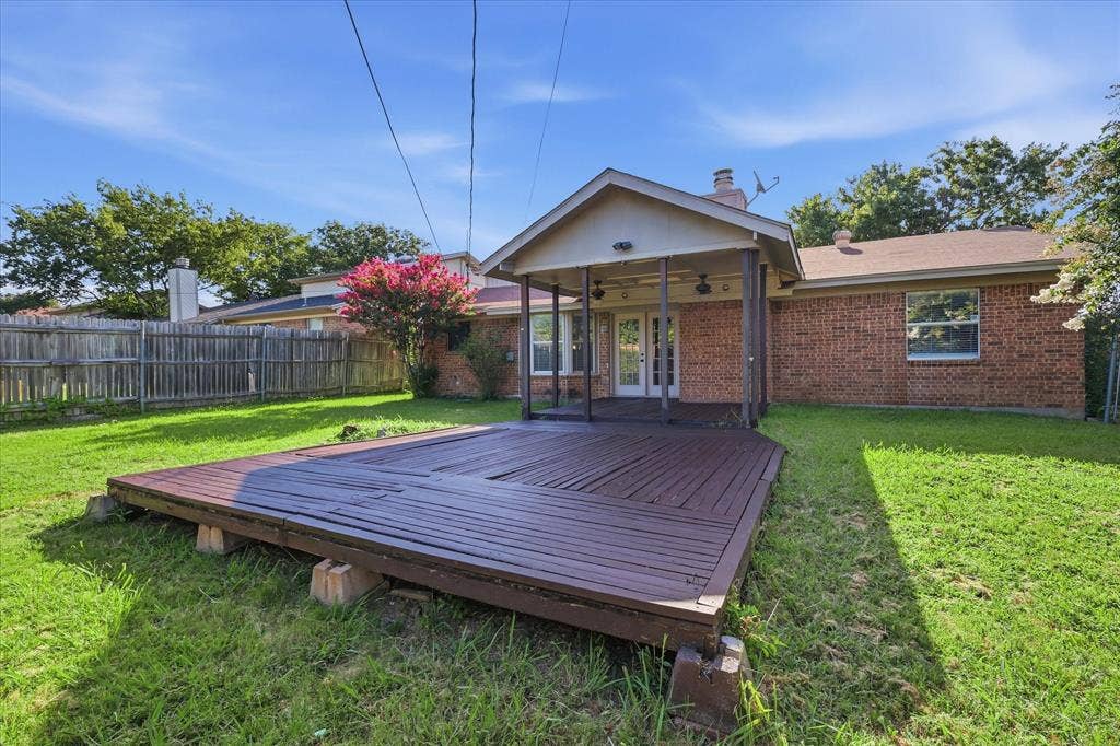 6505 Hughes Drive, Watauga, TX 76148 Expansive backyard featuring a large wooden deck, covered patio, brick exterior, and lush green lawn