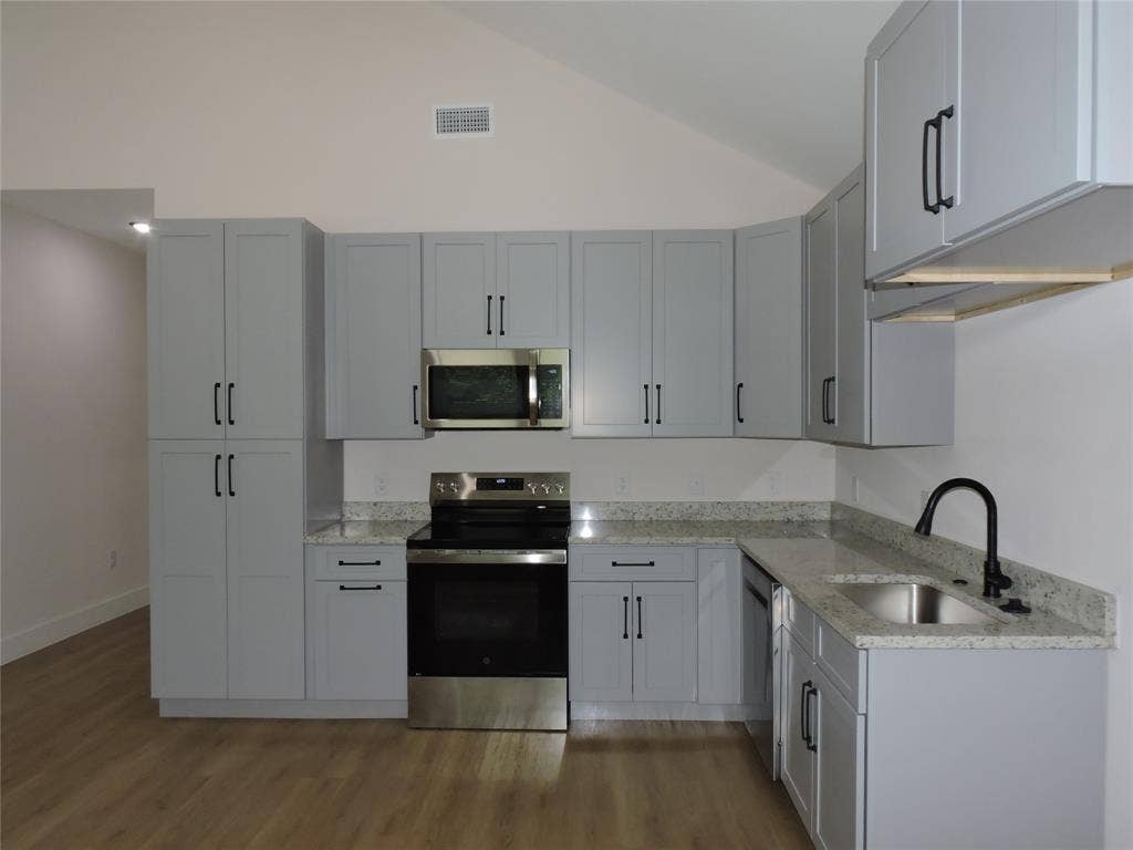 163 Lake Creek Drive, Mabank, TX 75156 Modern kitchen featuring light gray shaker-style cabinetry, stainless steel appliances, speckled countertops, a black gooseneck faucet, and wood-finish flooring