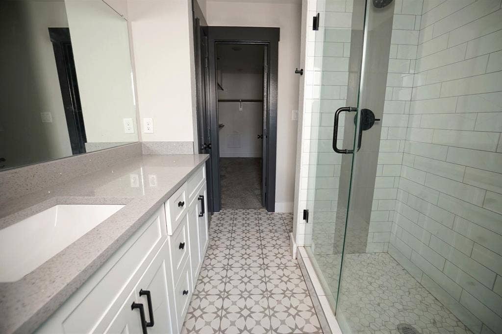 1764 Palladio Loop, Princeton, TX 75407 Dual vanity with gray quartz countertop, white cabinetry with black hardware, glass-enclosed shower with subway tile surround, and patterned floor tile