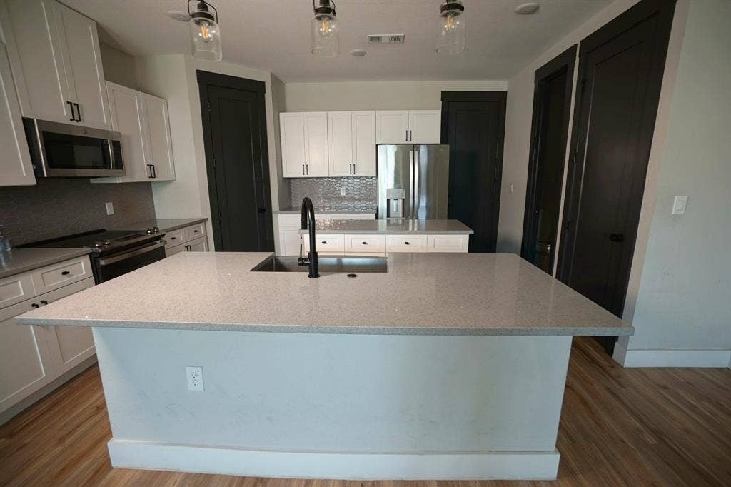 1764 Palladio Loop, Princeton, TX 75407 Kitchen featuring an island with an undermount sink, pendant lighting, stainless steel appliances, white cabinetry, and wood-finish flooring