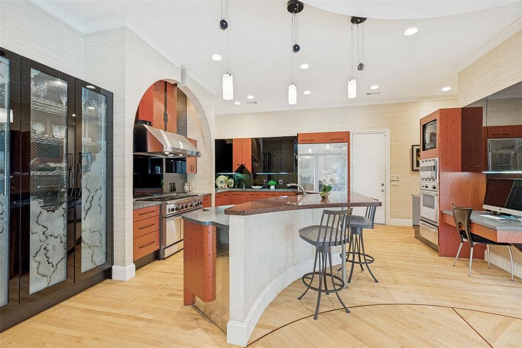 5920 Mcfarland Drive, Plano, TX 75093 Gourmet kitchen featuring a large curved island with a stone countertop, stainless steel appliances including a range and hood, custom wood cabinetry, and light wood-finish flooring
