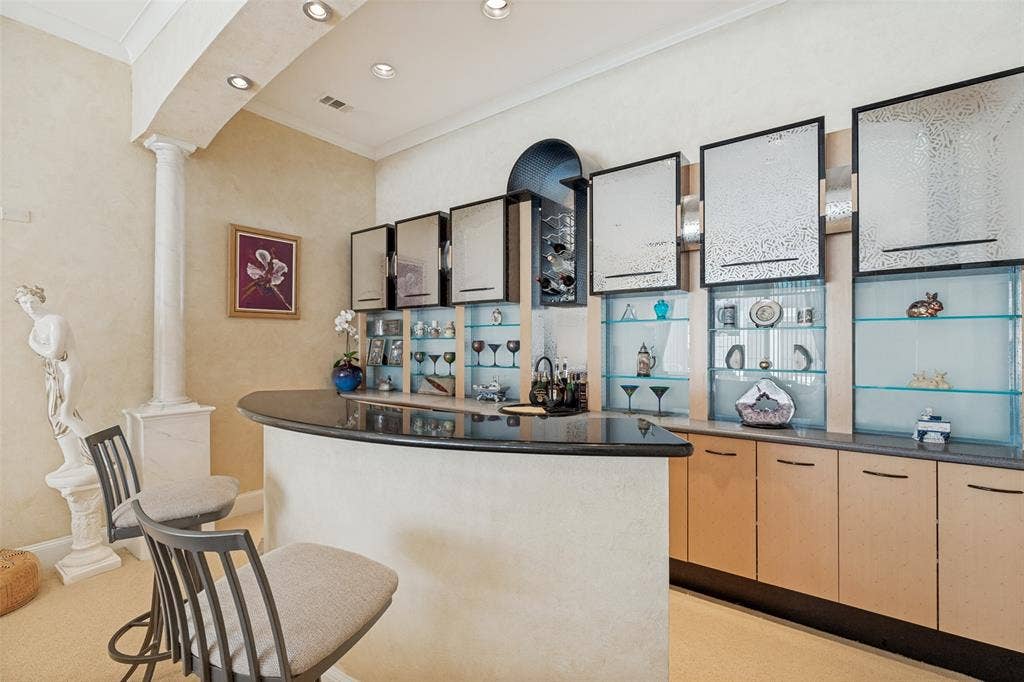 5920 Mcfarland Drive, Plano, TX 75093 Curved bar with a dark countertop and integrated shelving, featuring glass-front display cabinets, light wood-finish lower cabinetry, and recessed lighting
