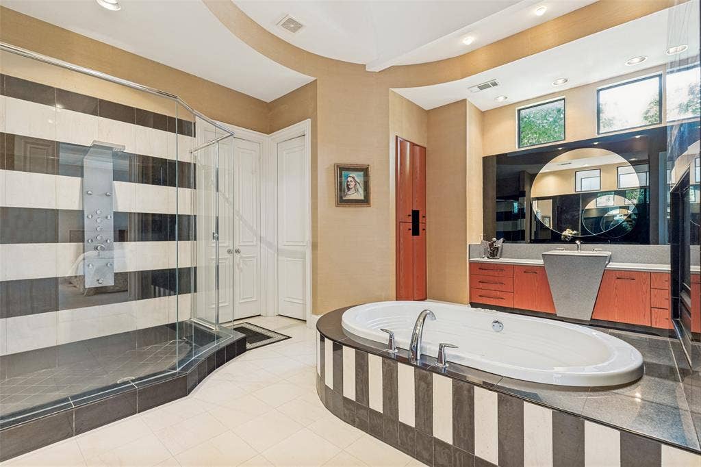 5920 Mcfarland Drive, Plano, TX 75093 Contemporary bathroom featuring a large soaking tub with integrated deck, a glass-enclosed shower with body jets, a pedestal sink, and a vanity with abundant cabinetry