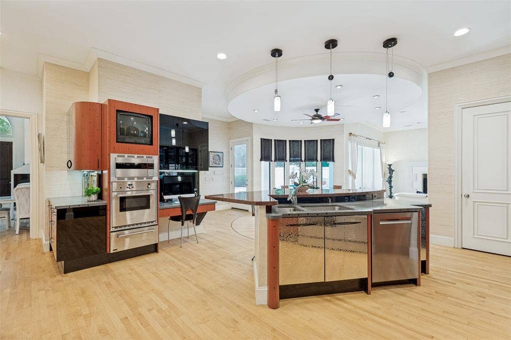 5920 Mcfarland Drive, Plano, TX 75093 Open-concept kitchen featuring wood-finish flooring, a built-in stainless steel oven and microwave combination, a curved island with integrated sink and dishwasher, and recessed lighting