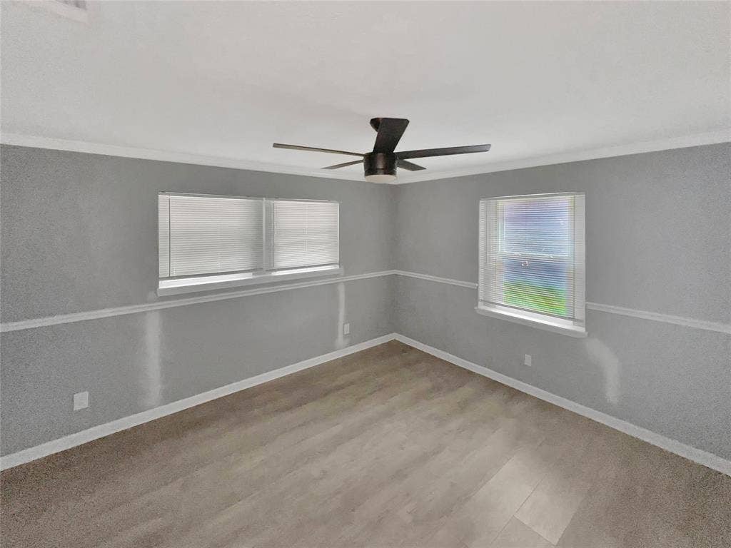 1306 Elby Street, Irving, TX 75061 Spacious room featuring wood-finish flooring, two windows with blinds, a modern ceiling fan, and grey walls with white trim