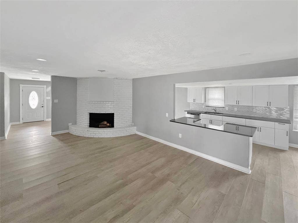 1306 Elby Street, Irving, TX 75061 Expansive living space featuring light wood-finish flooring and a white painted brick fireplace