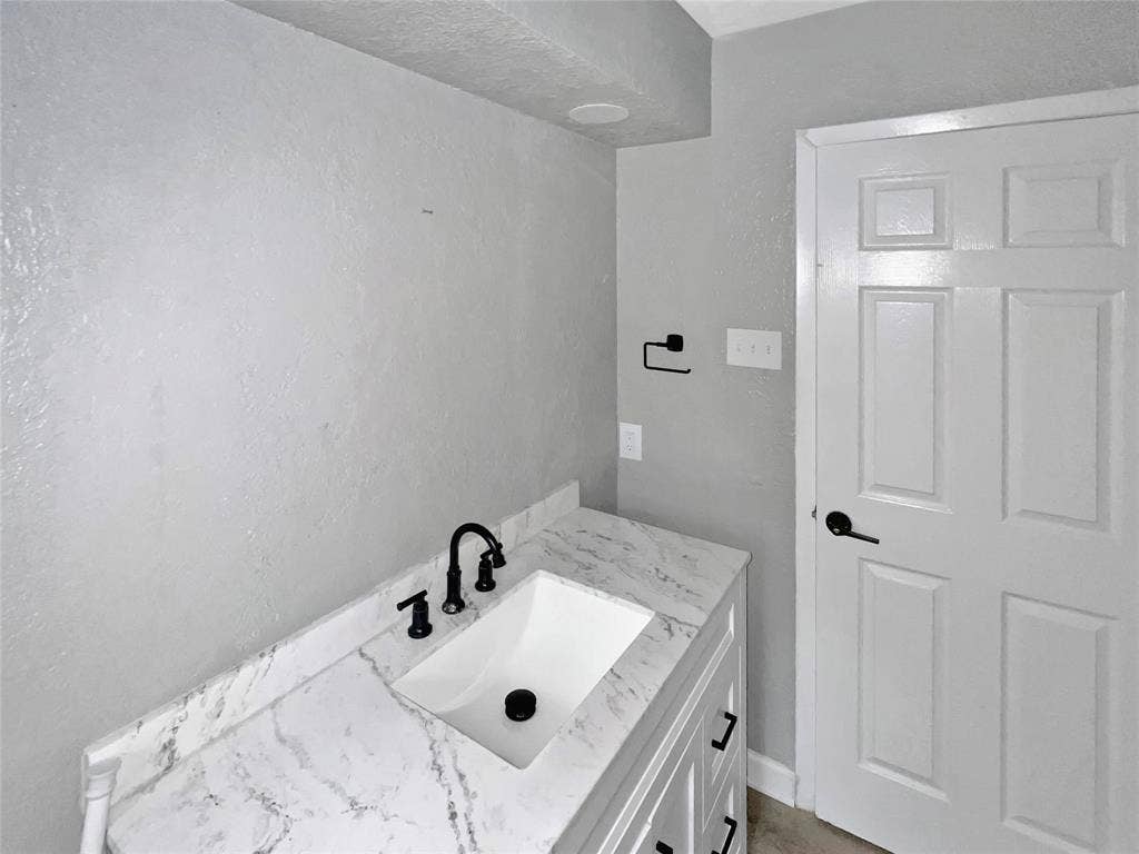 1306 Elby Street, Irving, TX 75061 White vanity featuring a built-in rectangular sink, black hardware, and a stone-finish countertop