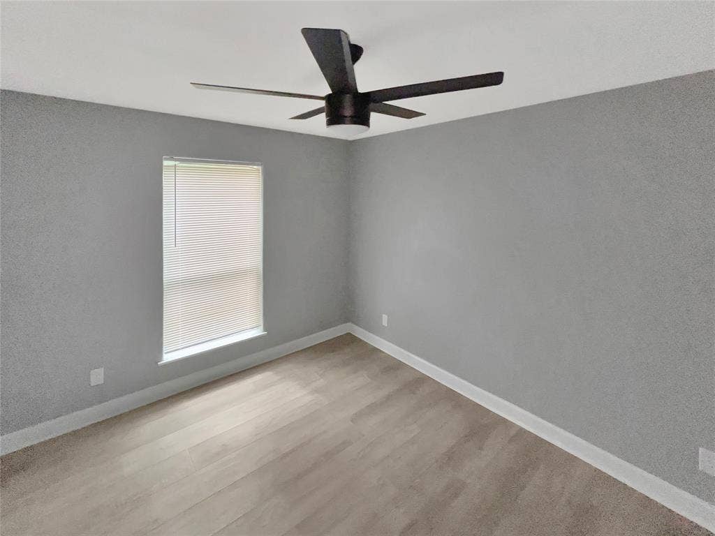 1306 Elby Street, Irving, TX 75061 Room featuring wood-finish flooring, a window with blinds, a ceiling fan with dark blades, and light gray walls with white baseboards