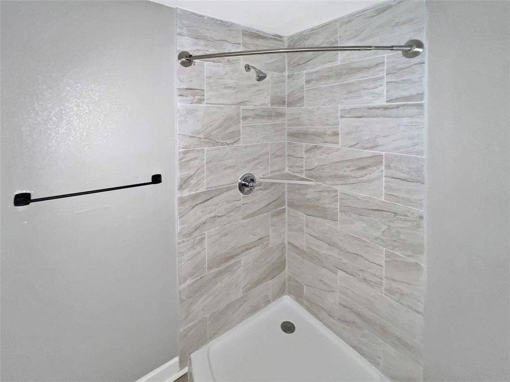 1306 Elby Street, Irving, TX 75061 Corner shower featuring light-toned tilework with a varied pattern, a built-in shower niche, and a contrasting matte black towel bar
