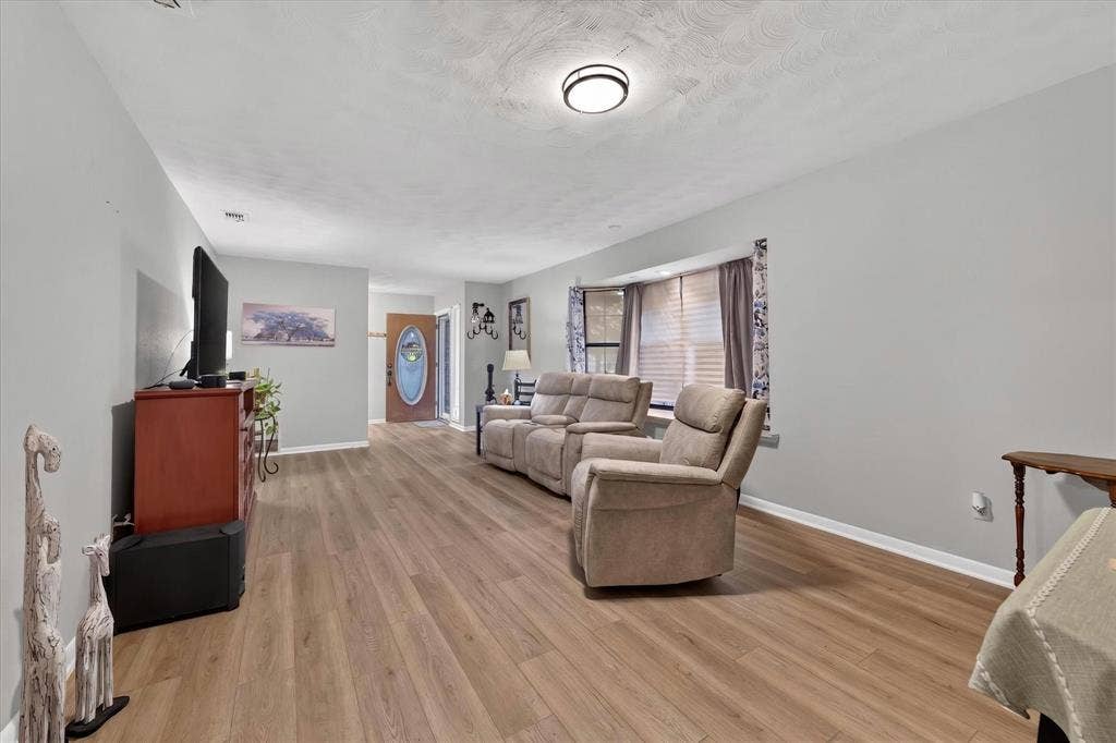 9700 Brookwood Circle, Woodway, TX 76712 Spacious living area featuring wood-finish flooring, light gray walls, and a recessed bay window with blinds