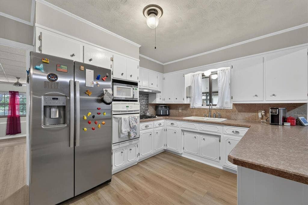 9700 Brookwood Circle, Woodway, TX 76712 Kitchen featuring wood-finish flooring, white cabinetry, a built-in oven, and a stainless steel refrigerator
