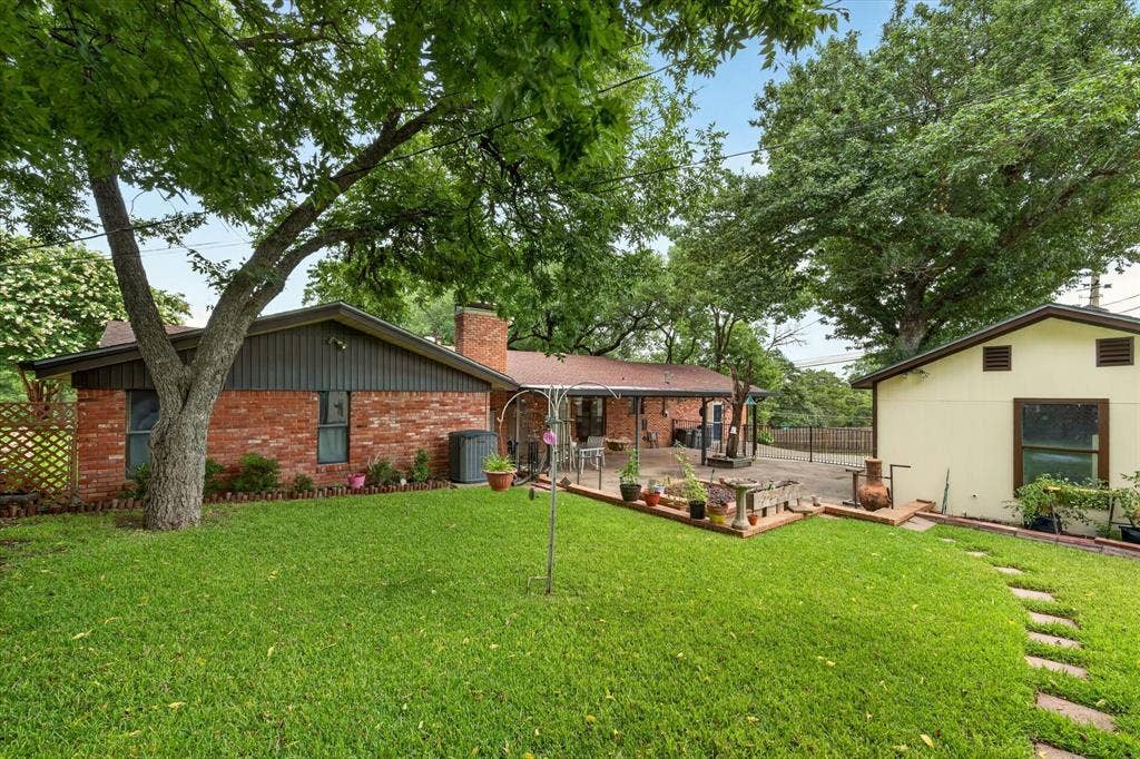 9700 Brookwood Circle, Woodway, TX 76712 Spacious backyard featuring a lush lawn, mature trees, brick patio, and a separate structure with a light-colored exterior