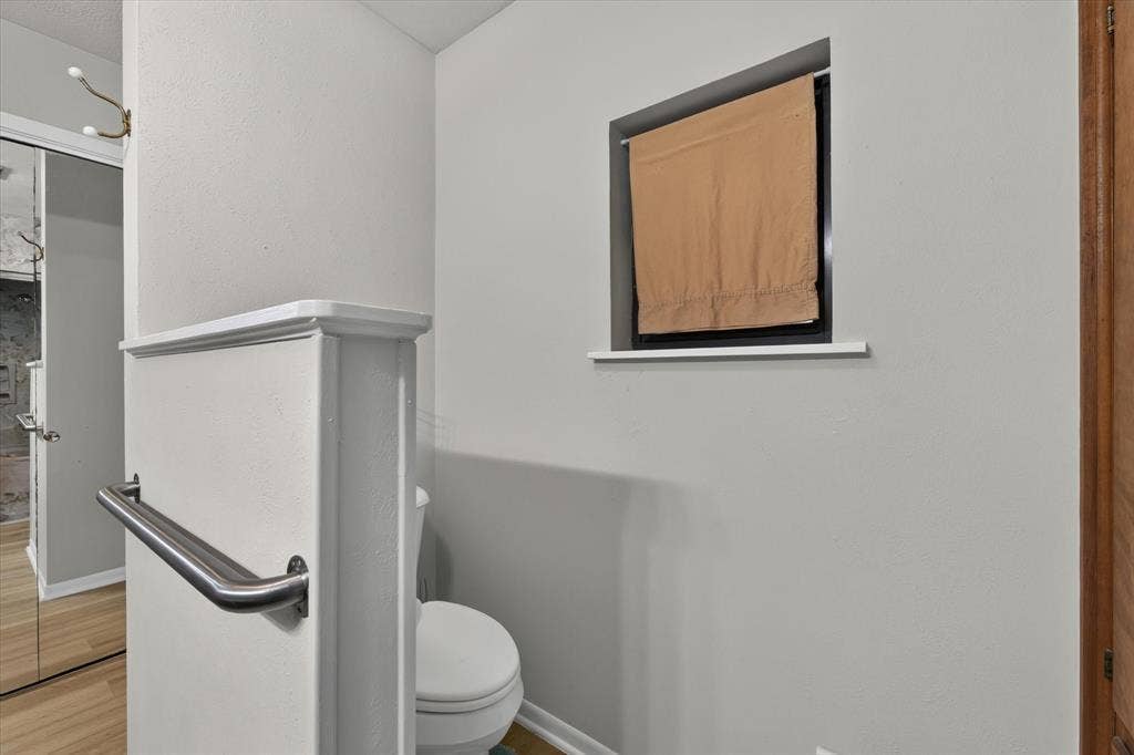 9700 Brookwood Circle, Woodway, TX 76712 Compact water closet featuring a white toilet, light gray painted walls, and a built-in window with a ledge