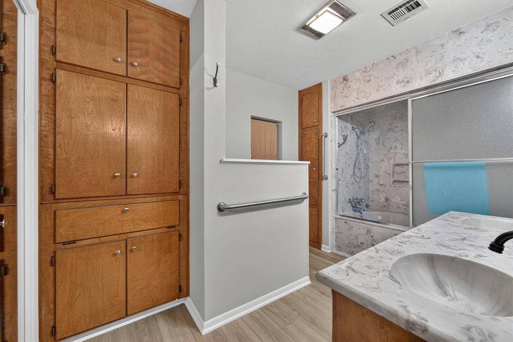 9700 Brookwood Circle, Woodway, TX 76712 Bathroom featuring a built-in wood-finish storage cabinet, a vanity with an integrated sink and patterned countertop, and a shower-over-tub combination with a sliding glass enclosure