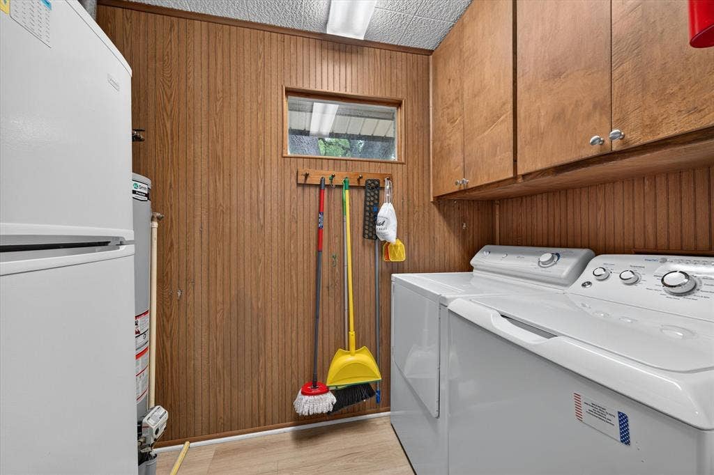 9700 Brookwood Circle, Woodway, TX 76712 Utility room featuring wood-finish wall paneling, light wood-finish flooring, and upper cabinetry