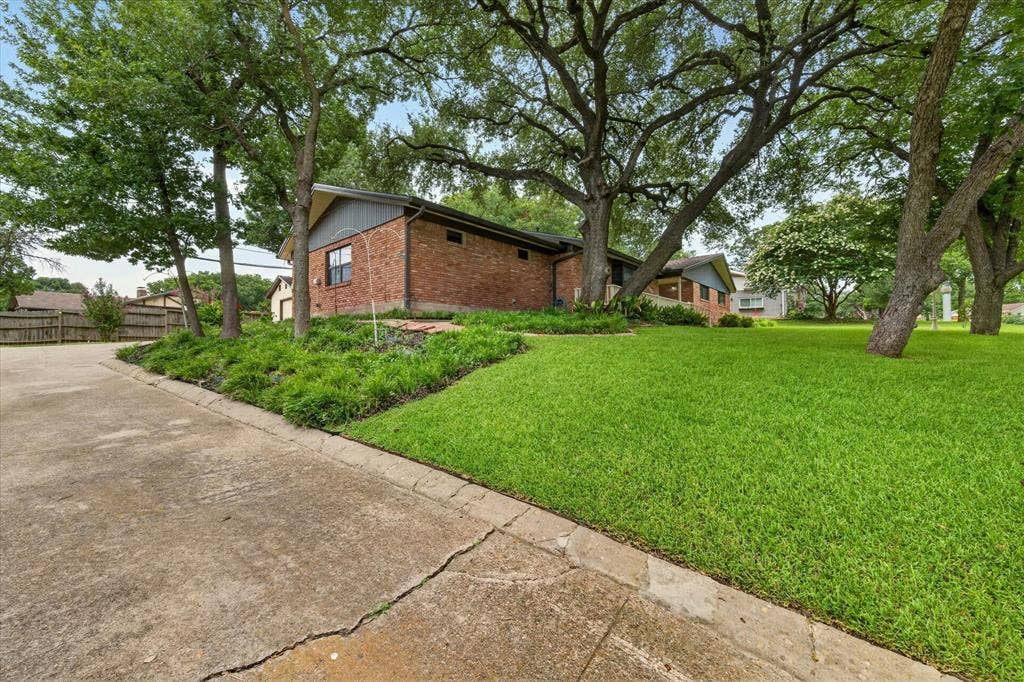 9700 Brookwood Circle, Woodway, TX 76712 Brick exterior with a gabled roofline, mature trees, landscaped shrubbery, and an expansive lawn area