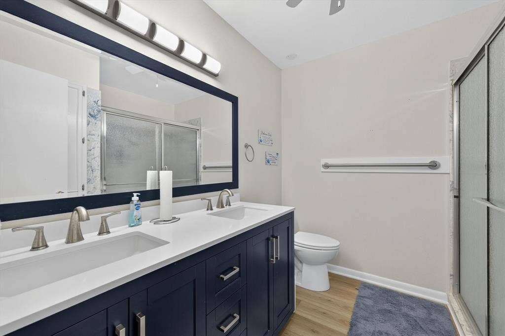 9700 Brookwood Circle, Woodway, TX 76712 Dual-sink vanity with a white countertop and navy cabinetry, brushed nickel hardware, a framed mirror, and a glass-enclosed shower