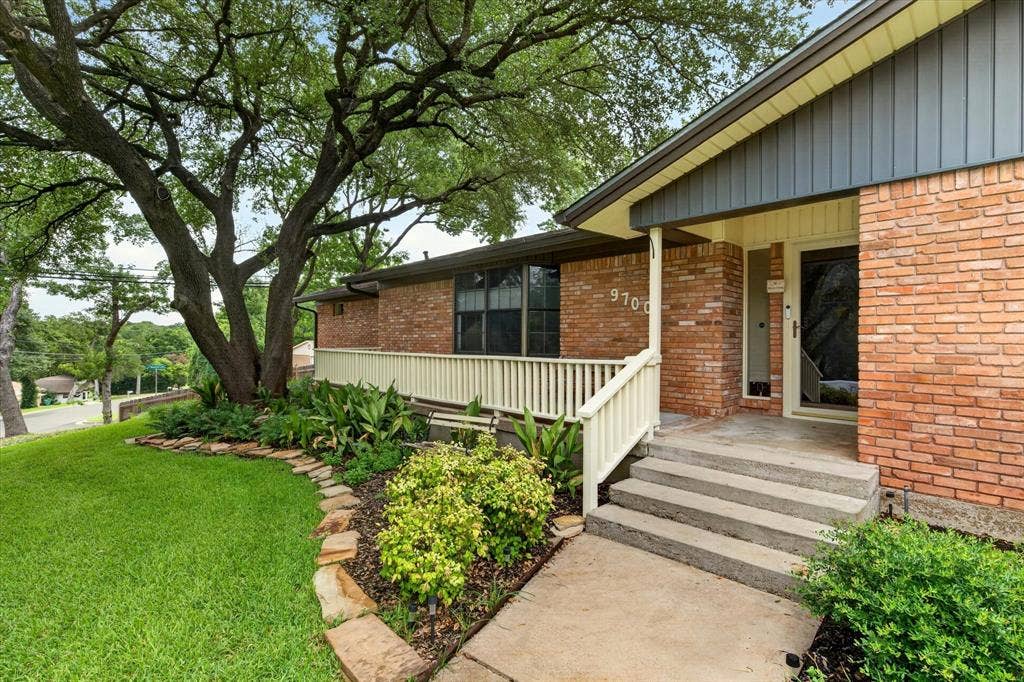 9700 Brookwood Circle, Woodway, TX 76712 Brick exterior with dark gray vertical siding accents, concrete walkway, and stone-edged landscaping