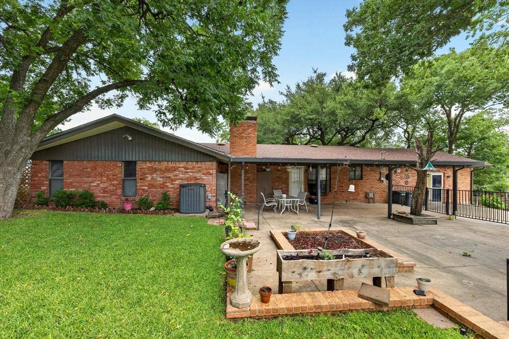 9700 Brookwood Circle, Woodway, TX 76712 Brick exterior featuring a covered patio, a spacious concrete pad, a raised planter, and mature trees providing natural shade