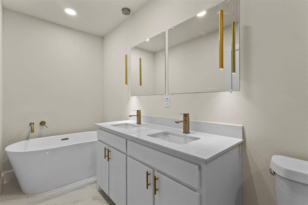 1104 S Brighton Avenue, Dallas, TX 75208 Freestanding soaking tub, dual vanity with undermount sinks, quartz countertops, brushed brass fixtures, and wall-mounted mirrors with integrated lighting