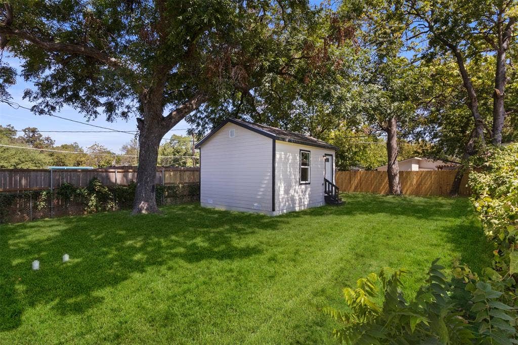 1104 S Brighton Avenue, Dallas, TX 75208 Expansive lawn featuring mature trees, a privacy fence, and an auxiliary structure with white siding and dark trim