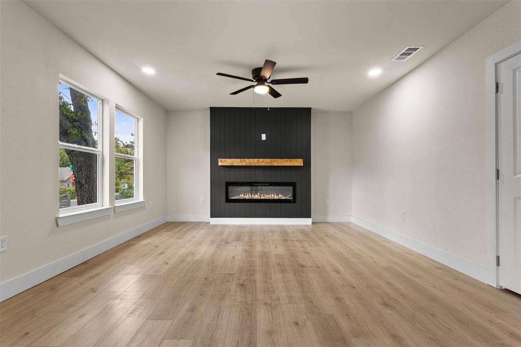 1104 S Brighton Avenue, Dallas, TX 75208 Wood-finish flooring, recessed lighting, and a dark shiplap accent wall with an electric fireplace and wood mantel