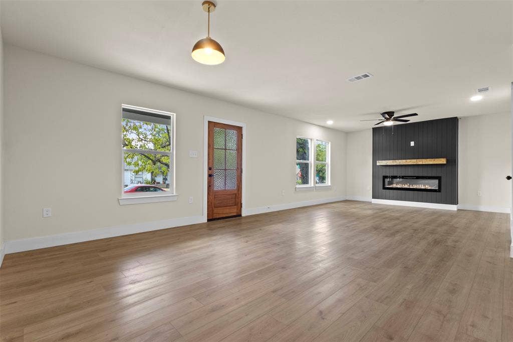 1104 S Brighton Avenue, Dallas, TX 75208 Expansive living area featuring light wood-finish flooring, a modern linear fireplace with a wood mantel, a black vertical slat accent wall, and recessed lighting