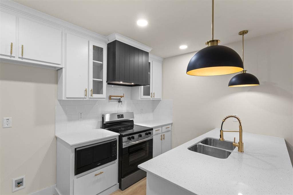1104 S Brighton Avenue, Dallas, TX 75208 Kitchen featuring white cabinetry, a black range hood, stainless steel appliances, a double basin sink with a gold-finish faucet, and pendant lighting