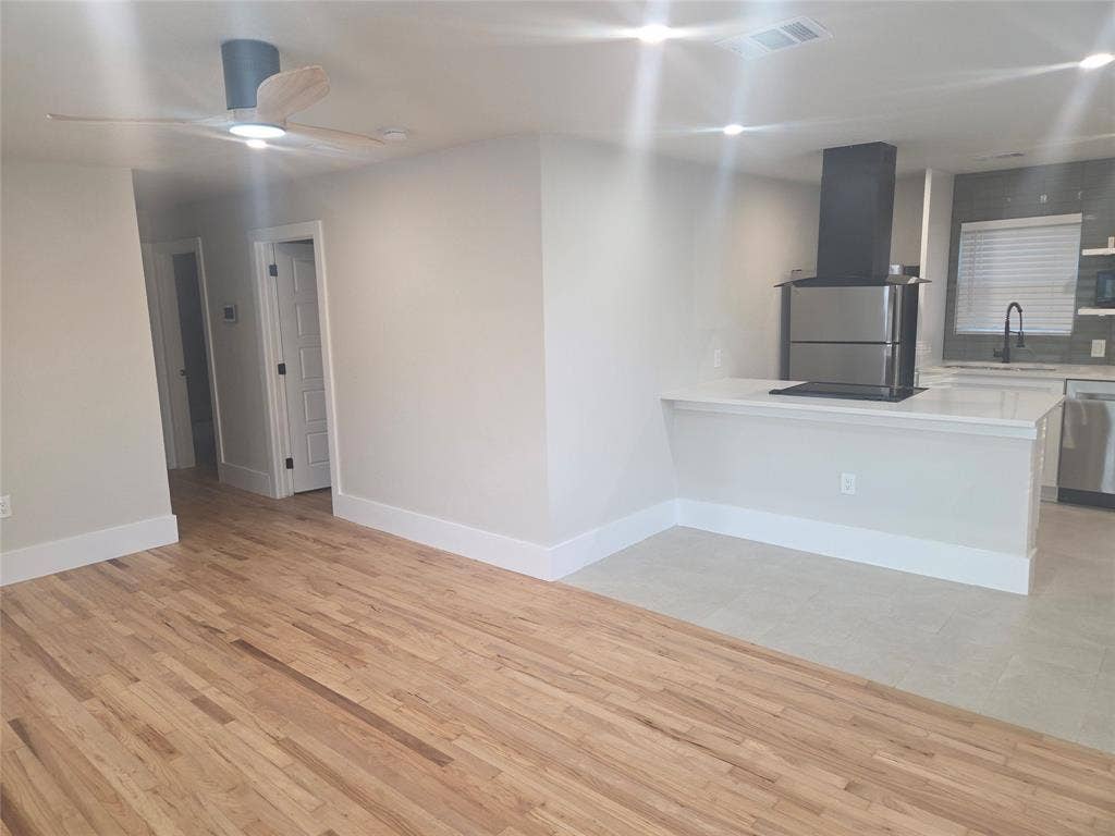2329 Cass Street, Fort Worth, TX 76112 Open-concept living space featuring wood-finish flooring, a modern ceiling fan with lighting, and a kitchen peninsula with a cooktop and integrated downdraft ventilation
