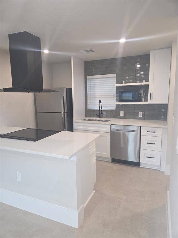 2329 Cass Street, Fort Worth, TX 76112 Modern kitchen featuring an island with an integrated cooktop, a black range hood, stainless steel appliances, white cabinetry, and gray subway tile backsplash