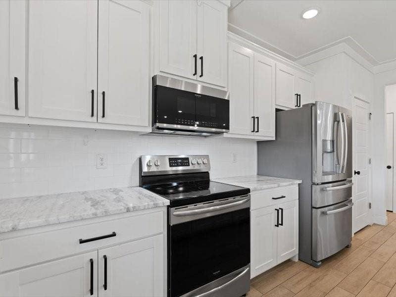 5528 Mesa Loop, Granbury, TX 76048 Kitchen featuring white shaker-style cabinetry with matte black hardware, stainless steel appliances, a subway tile backsplash, and light-toned countertops