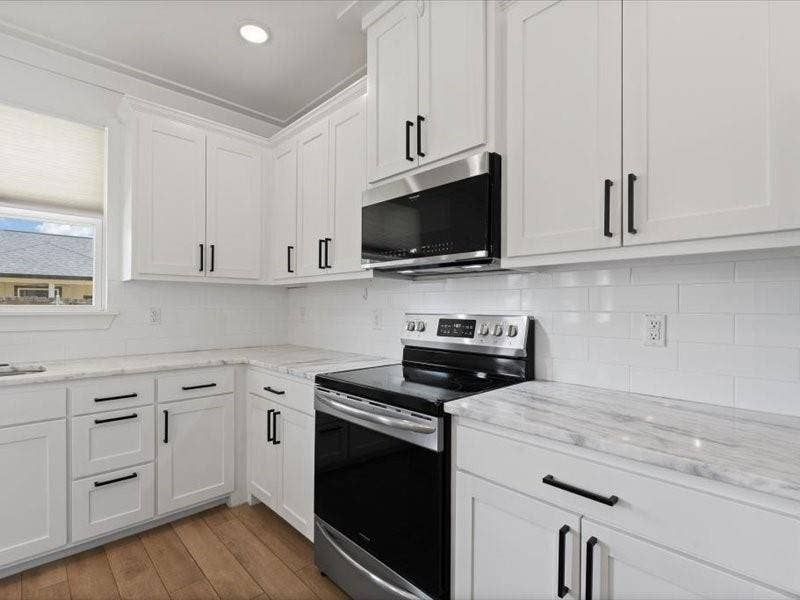 5528 Mesa Loop, Granbury, TX 76048 Kitchen featuring white cabinetry with matte black hardware, stone countertops with subtle veining, a white subway tile backsplash, stainless steel appliances, and wood-finish flooring