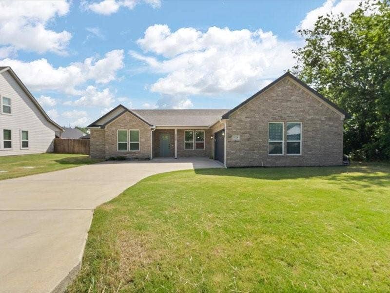 5528 Mesa Loop, Granbury, TX 76048 Brick veneer exterior with a contrasting teal entry door, a multi-car concrete driveway, a gabled roofline, and an integrated garage