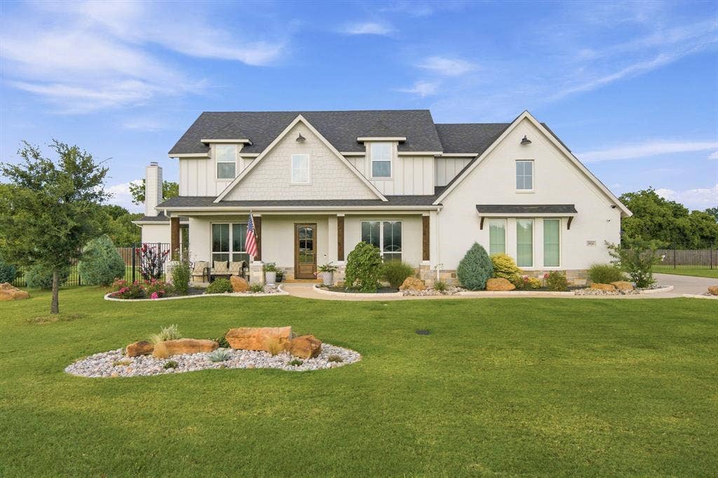 White stucco exterior with dark shingle roofing, featuring a covered front porch with dark wood columns