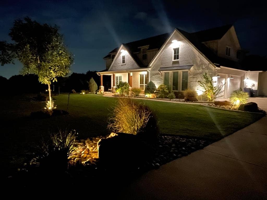 Exterior with multiple gables, covered front porch, attached garage, and extensive landscape lighting