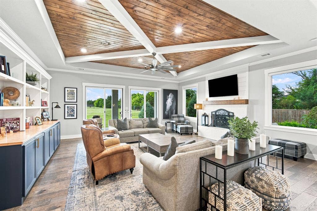 Vaulted wood-plank ceiling with beams, built-in shelving with lower cabinetry, sliding glass doors, white brick fireplace, and wood-finish flooring