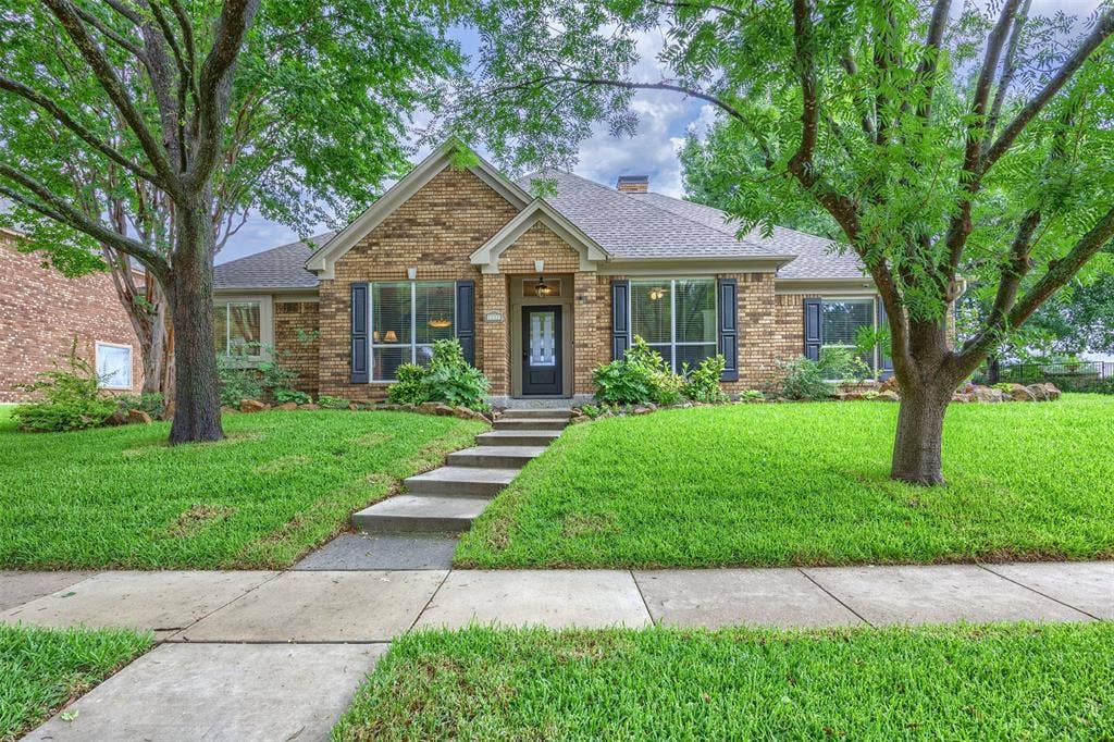 1717 Whitney Drive, Richardson, TX 75082 Brick facade residence featuring a stepped concrete walkway, mature trees, and a landscaped front yard