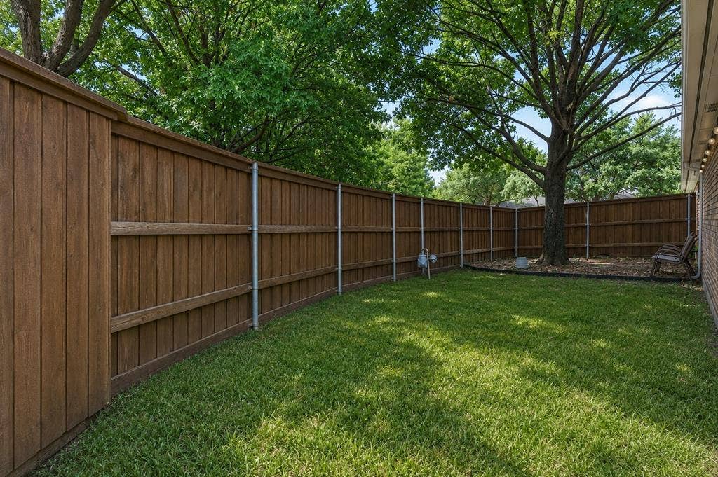 1717 Whitney Drive, Richardson, TX 75082 Private backyard featuring a full wood-panel fence, established tree providing natural shade, and a manicured lawn